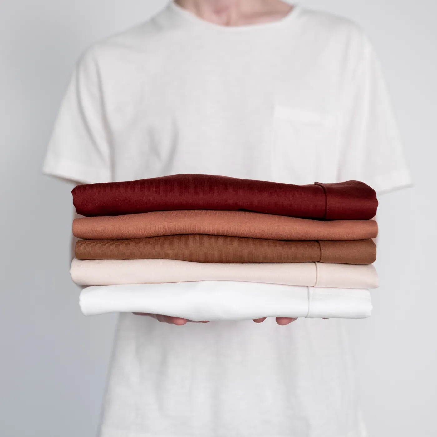 A person holding a neat stack of folded t-shirts in red, rust, tan and white