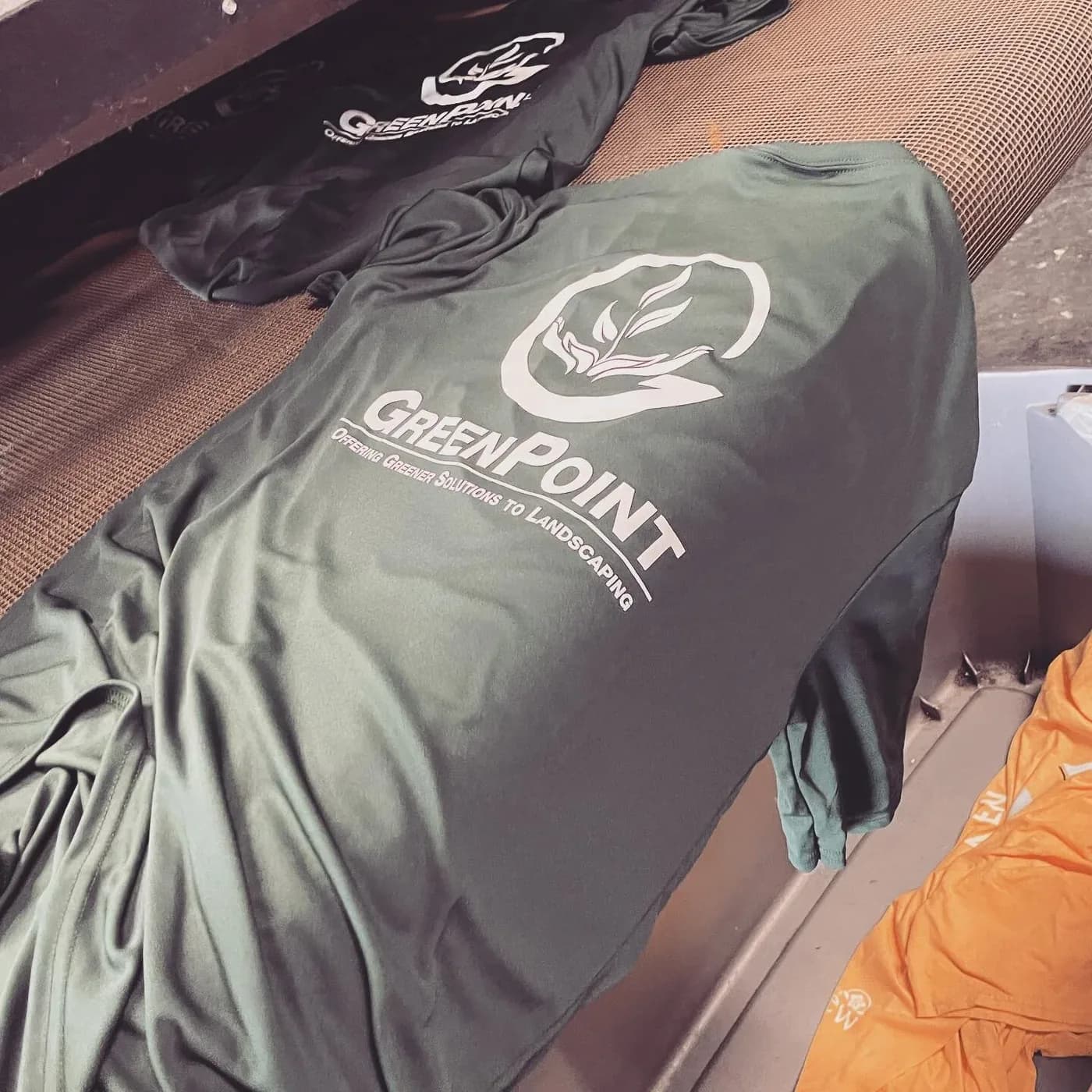 A dark printed work shirt on the press beside a stack of finished shirts