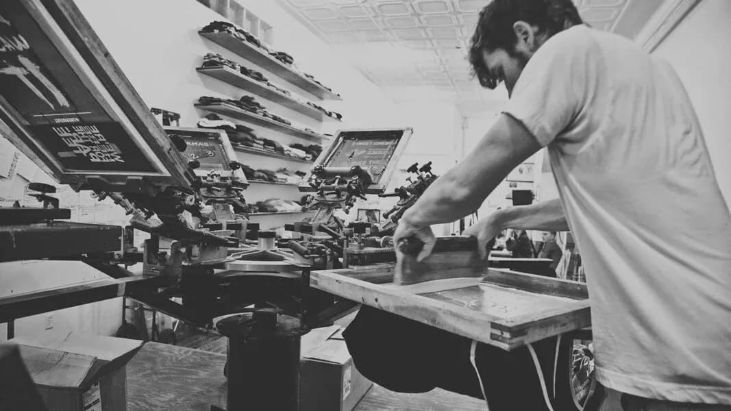Black and white photo of a CustomWear operator working at the manual screen printing carousel